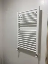 Radiador toallero blanco de pared en el baño de la habitación, visto en primer plano